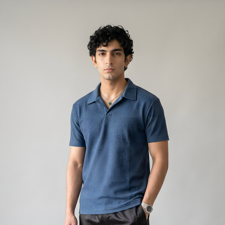 Man wearing a blue polo shirt and black pants with a logo, standing against a plain background