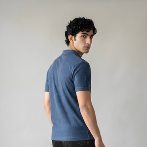 Man wearing a blue polo shirt and black pants against a plain background