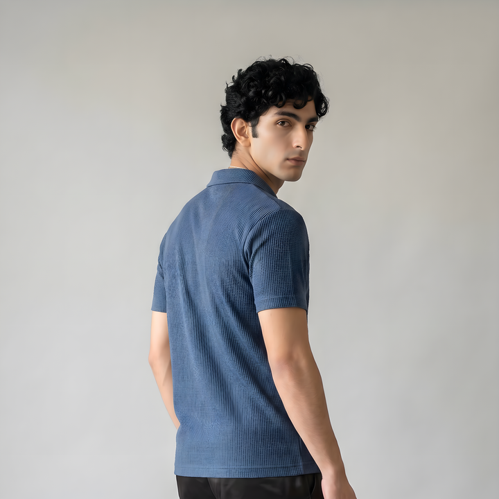 Man wearing a blue polo shirt and black pants against a plain background